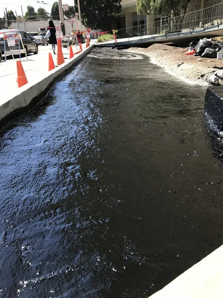 Black asphalt laid in a long, curved pathway, bordered by concrete and construction cones; sunny daytime.