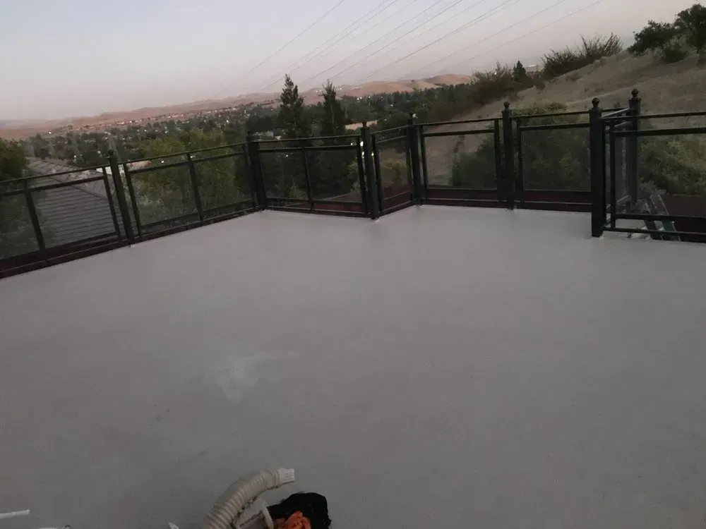 A gray concrete deck with black railing overlooking a distant city under a dusky sky.