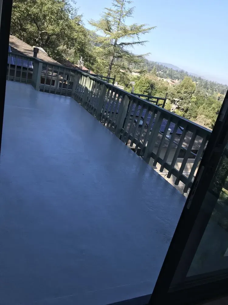 Deck with gray surface and railing, overlooking a mountainous landscape on a sunny day.