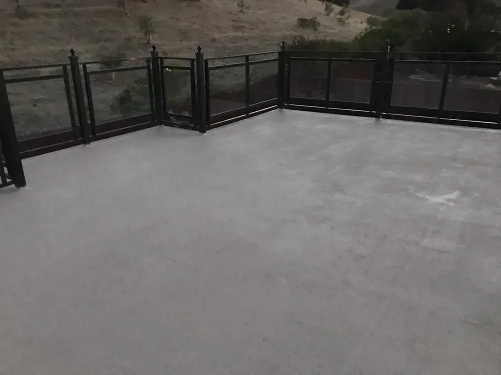 Outdoor concrete patio with black metal railing and a hillside view.