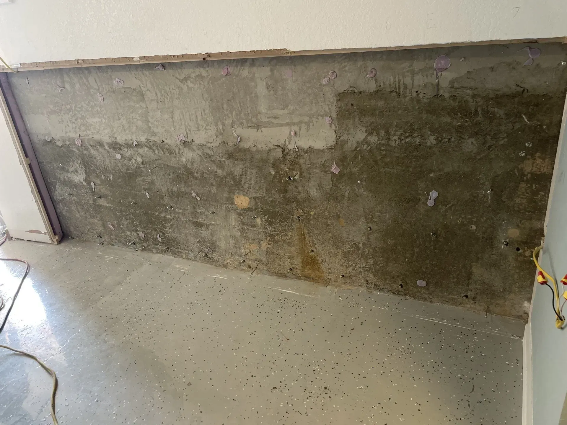 Concrete wall, partially stripped, exposed. Gray floor with speckles. Light coming from above.
