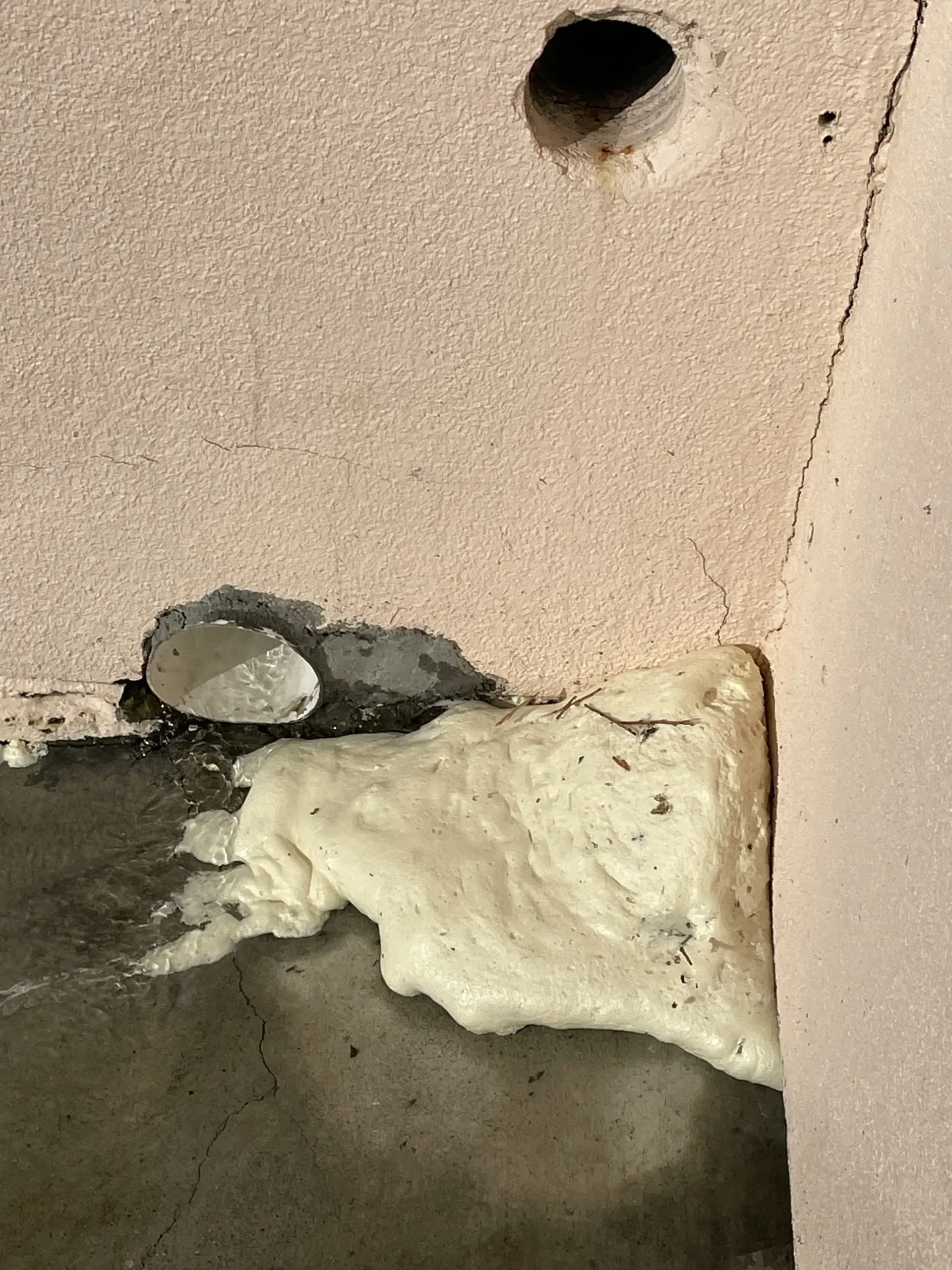 Foam insulation expanding around a concrete base. Hole in pink wall above.