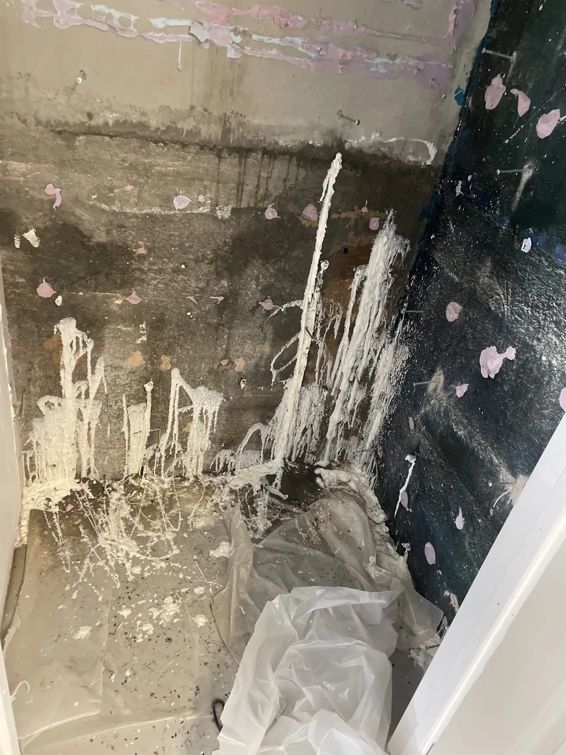 White splattered paint and plastic sheeting on a dark, wet surface, possibly a room under construction.