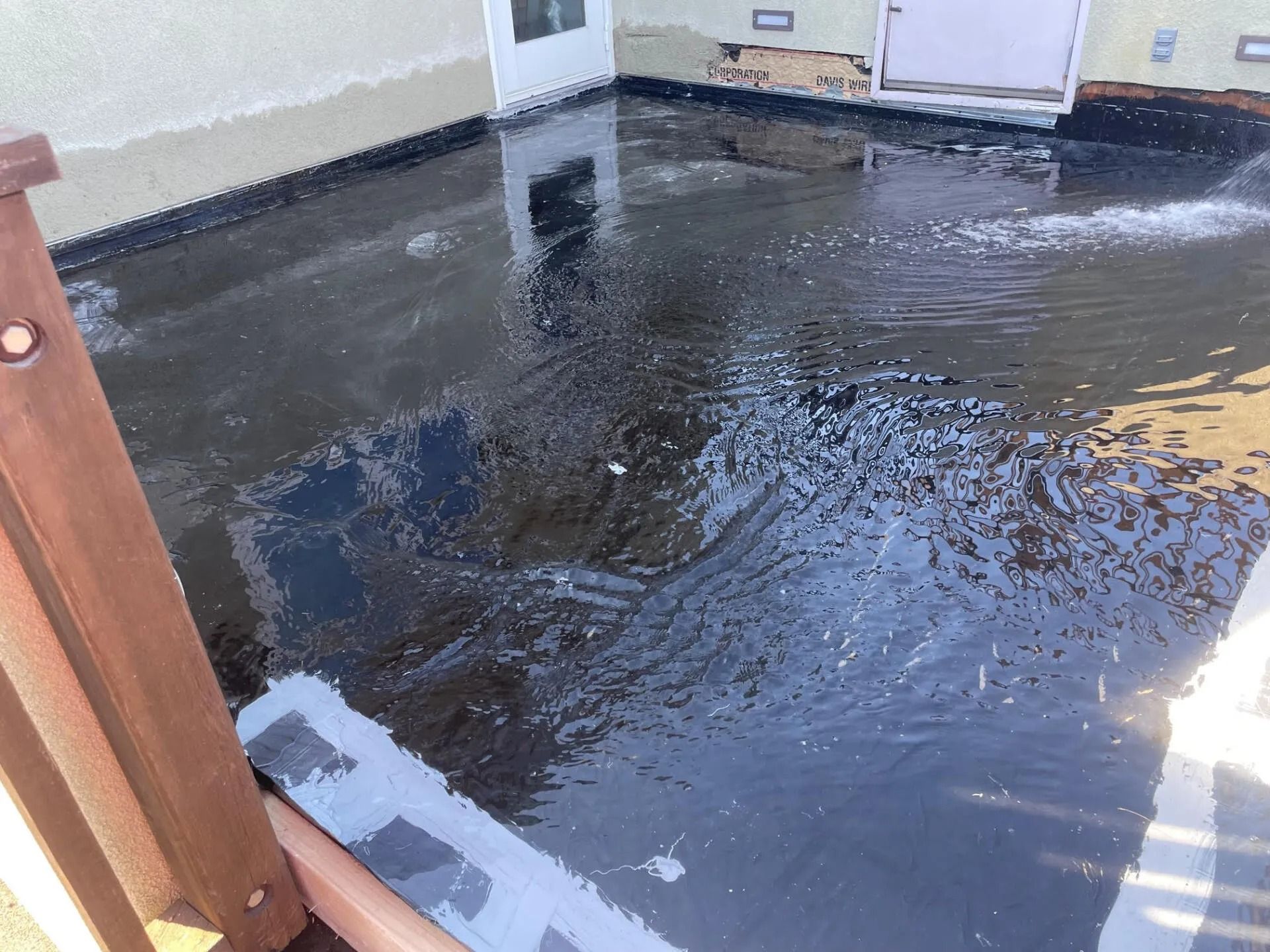 Water flowing on a black flat roof, next to a wooden railing.