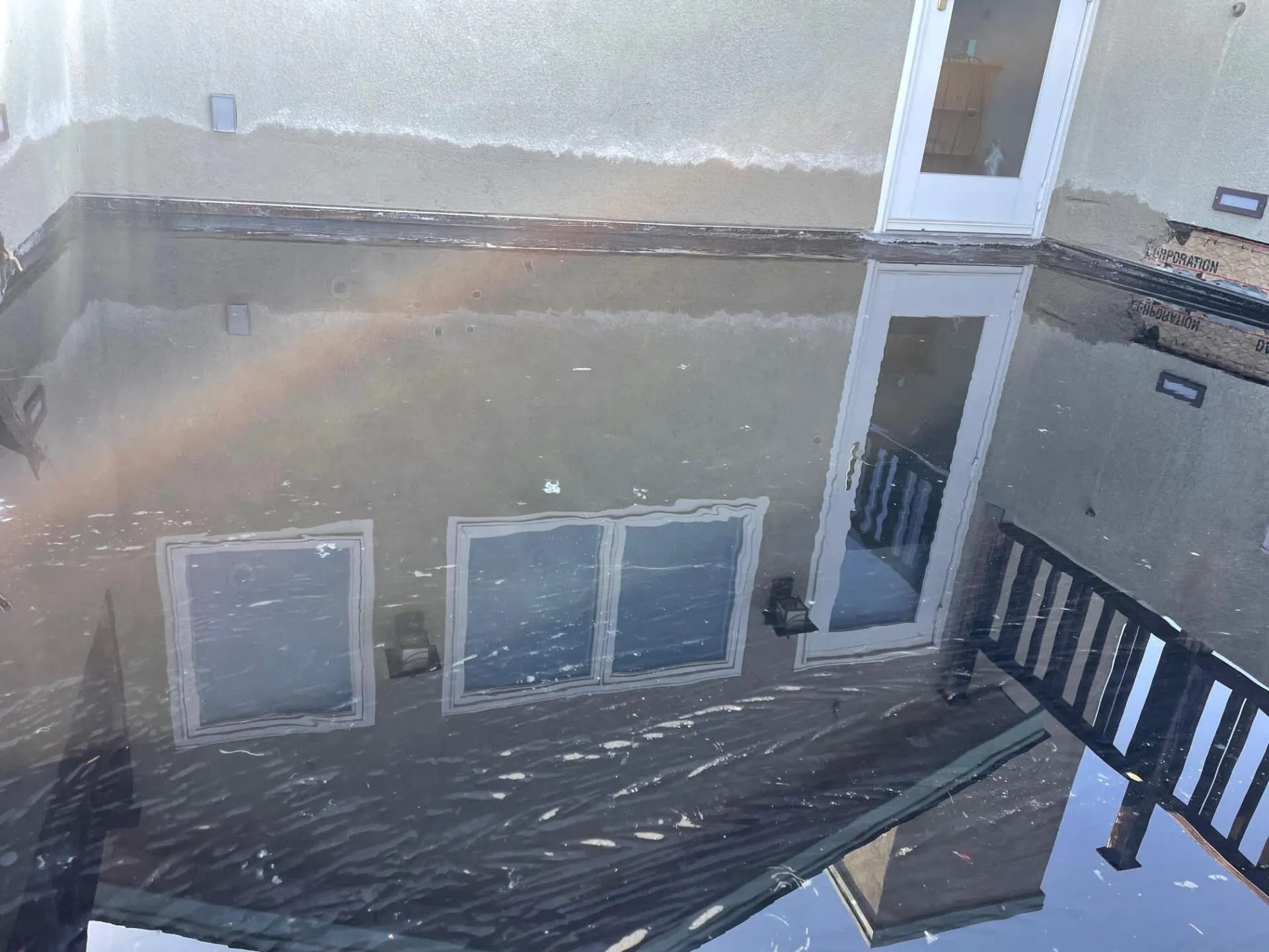 A house is reflected in standing water; visible are windows, a door, and a railing.