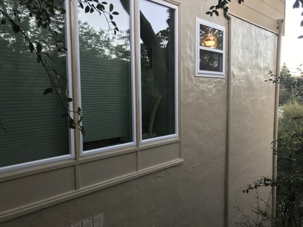 Exterior of a building with tan stucco walls, windows, and foliage.