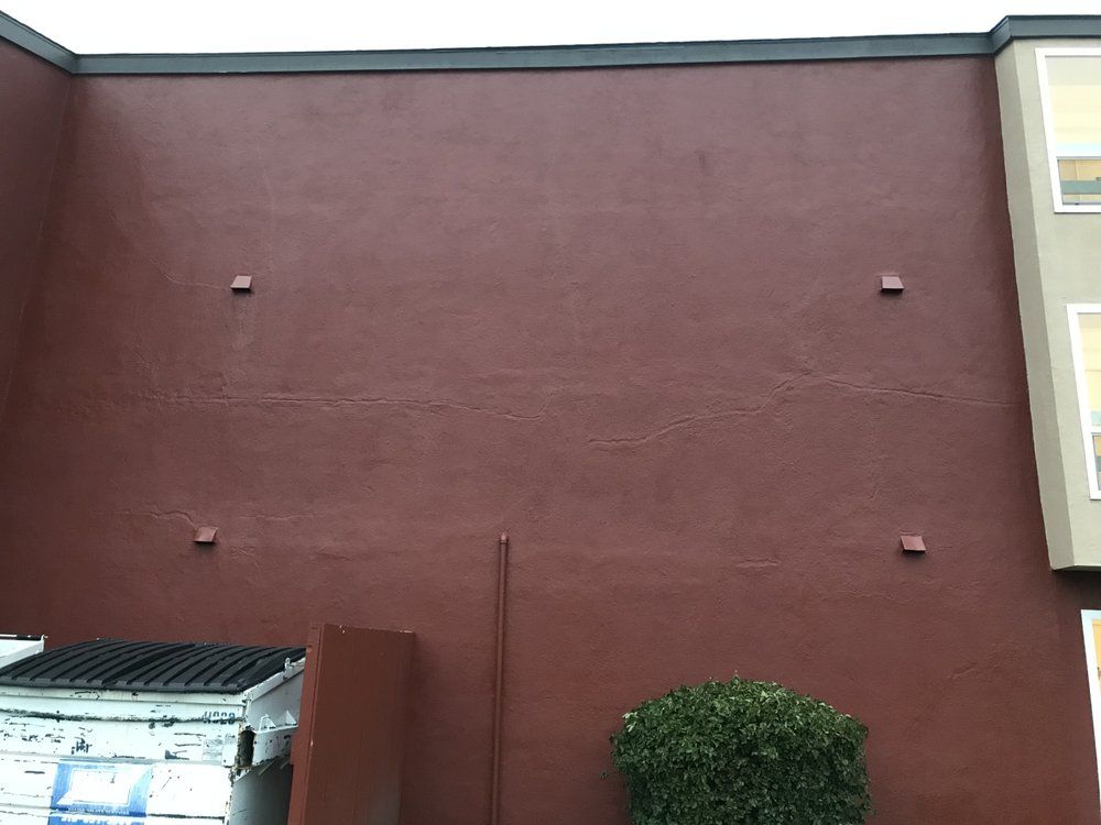 Red-painted building exterior with four square protrusions, a bush, and a trash bin.