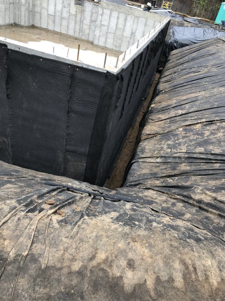 Foundation construction: black waterproof membrane lining a concrete structure. Earth surrounds.