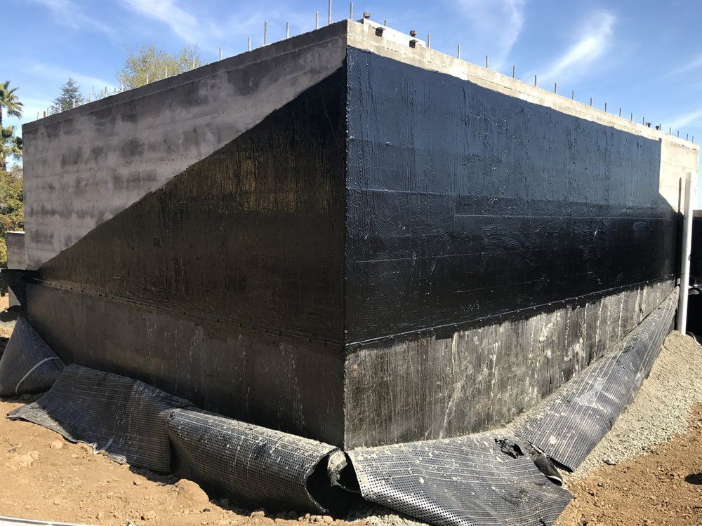 A concrete rectangular building with black waterproofing on its walls; black fabric surrounds the base; outdoors.