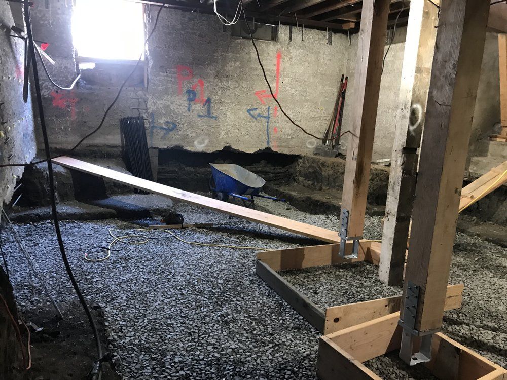 Basement construction site with wooden beams and gravel floor. A wheelbarrow sits in the background.