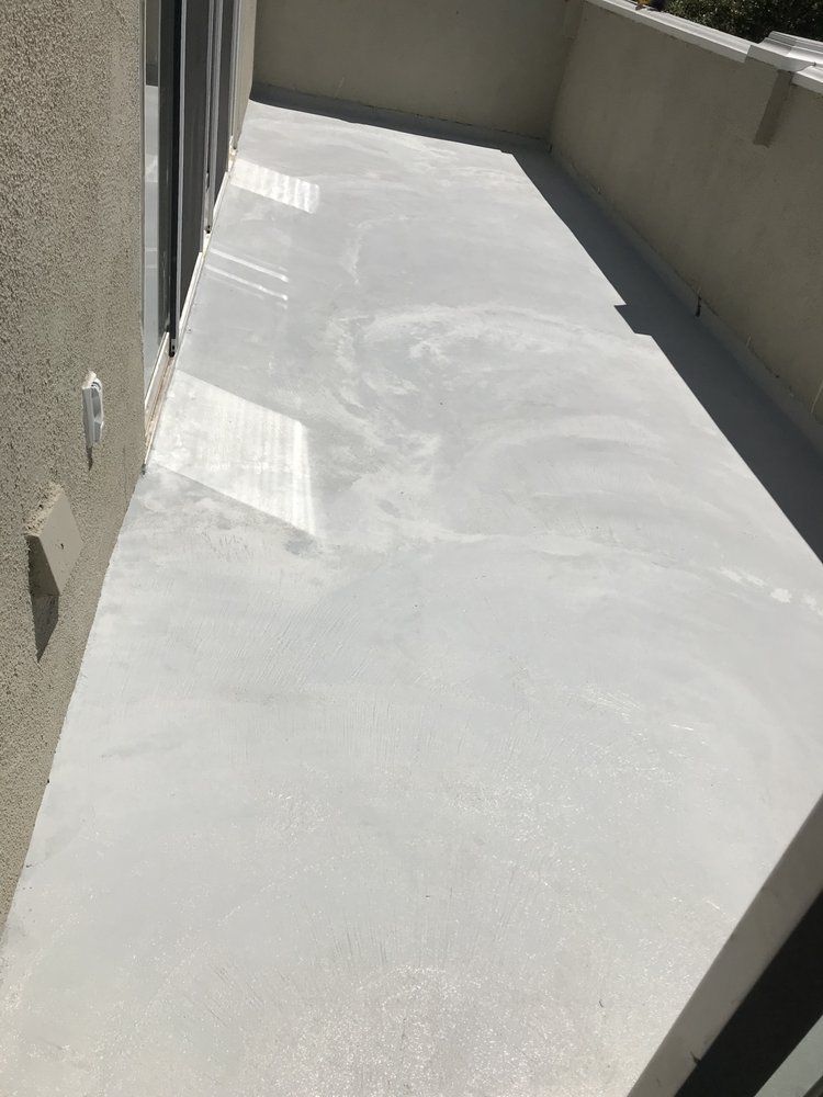 A narrow, white concrete balcony with sliding glass door and stucco wall.