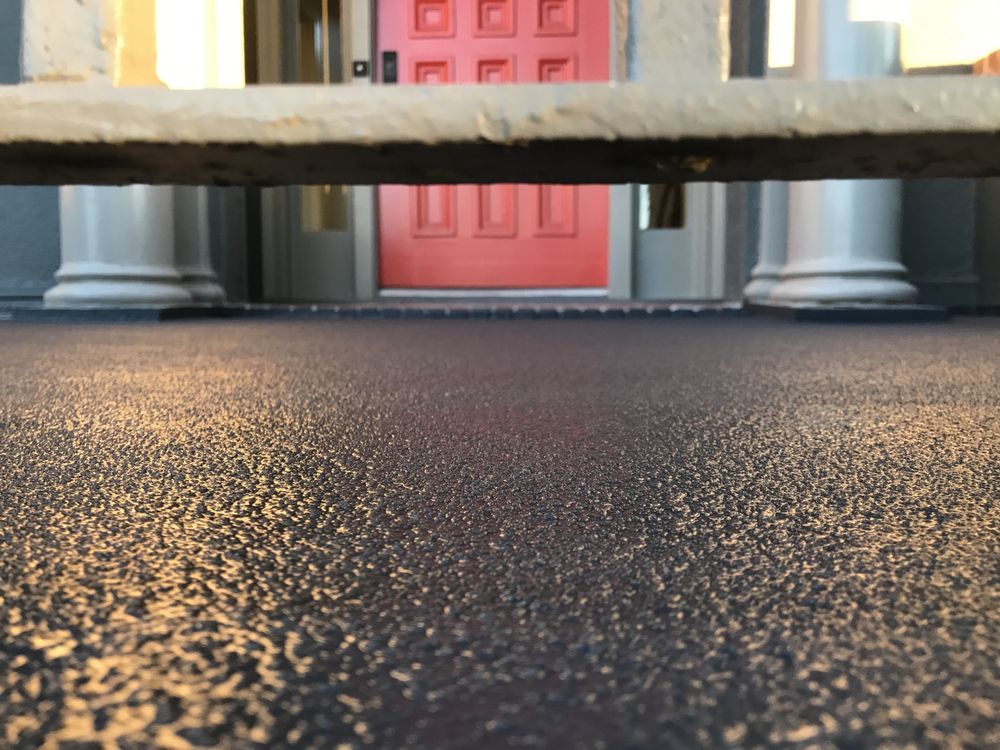 View through a railing: textured dark surface leads to a red door between white pillars.