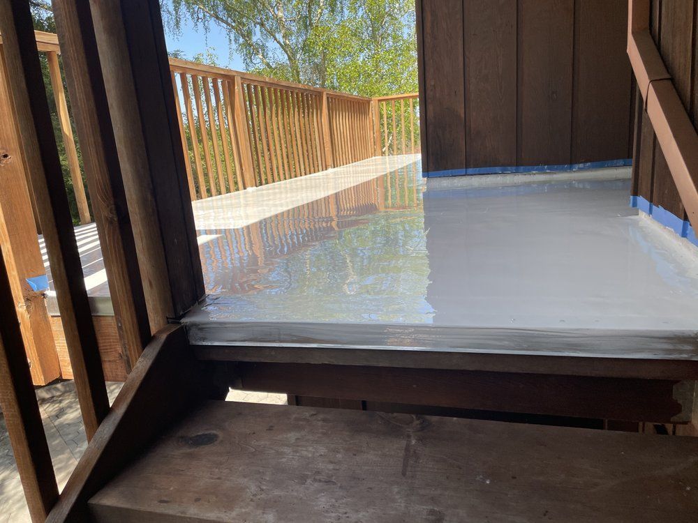 A wooden deck with freshly painted light gray surface, accessed by stairs. Brown railing and trim.