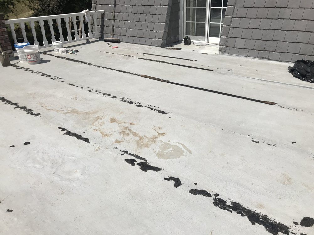 A flat, gray roof with dark lines and markings. A white railing and door are in the background.