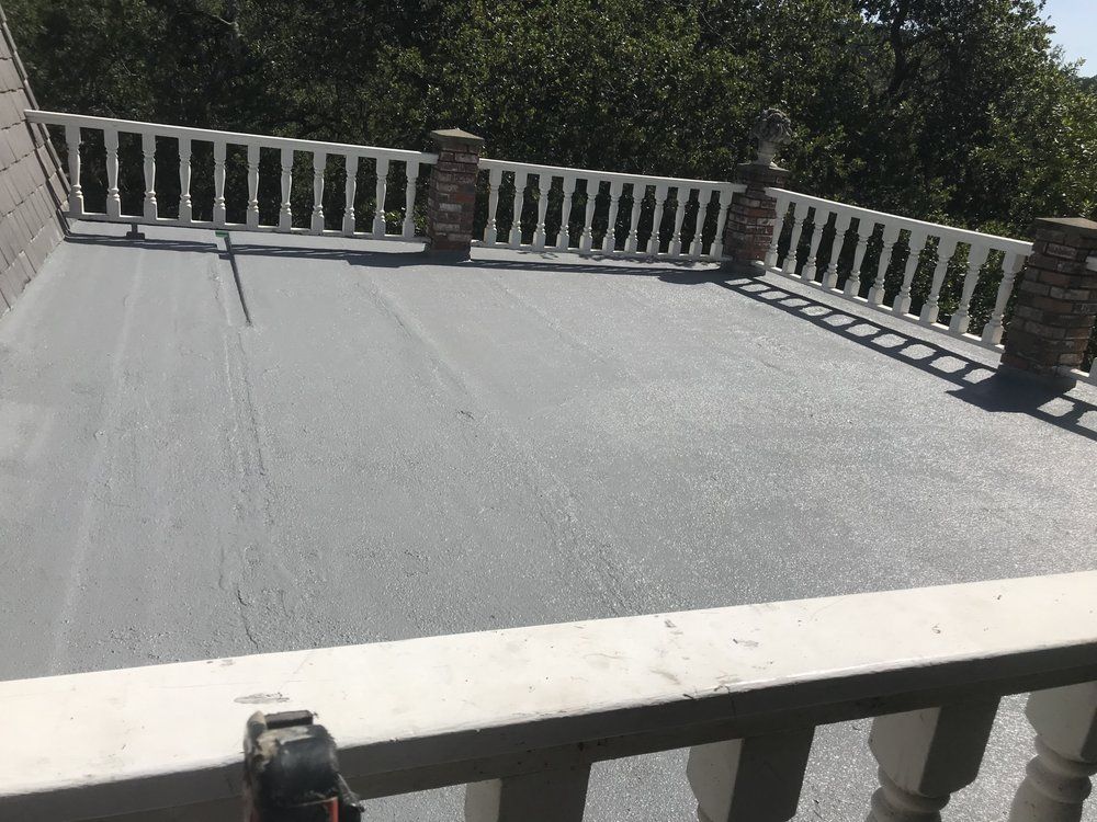 Gray, flat roof with white railing and brick posts. Trees in background.