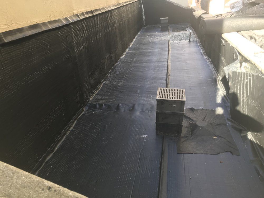 Black waterproof lining in a rectangular concrete structure. A drain grate is visible, with the space being prepared.
