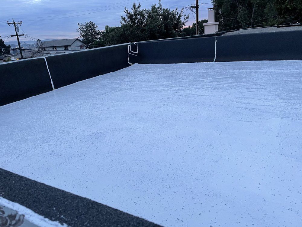 Flat roof coated in white, with black edging and drain pipes. Dusk setting, overcast sky.