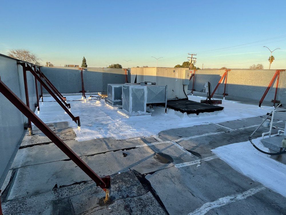 Rooftop with HVAC units and safety brackets, coated in a white material, under a clear sky.
