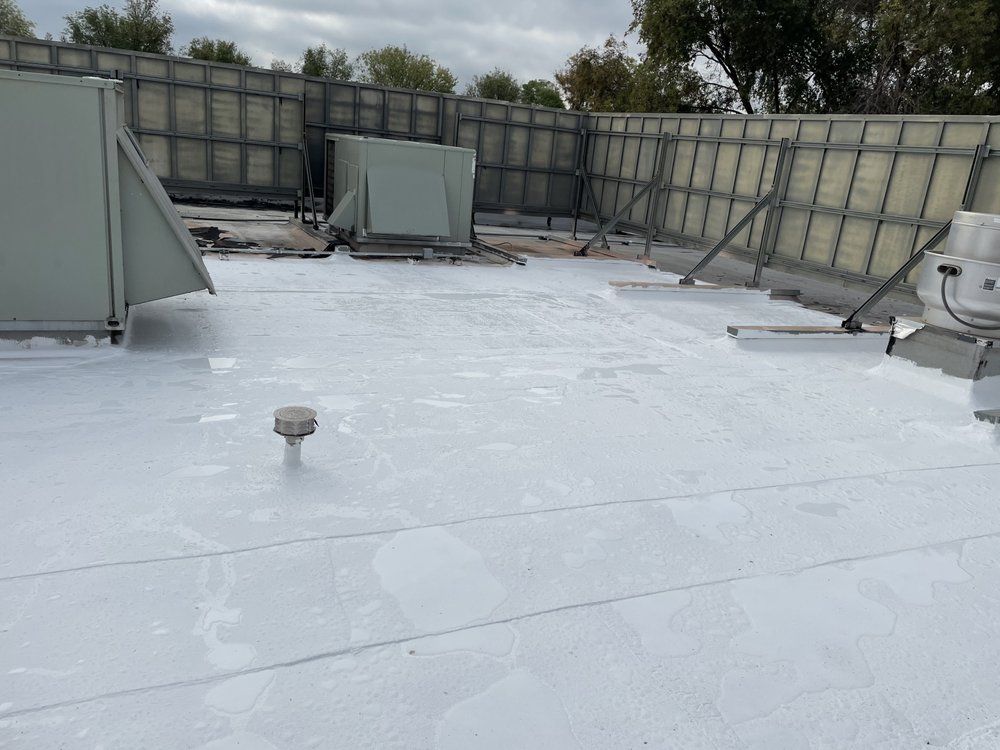 White-coated commercial rooftop with HVAC units, surrounded by metal panels. Overcast day.