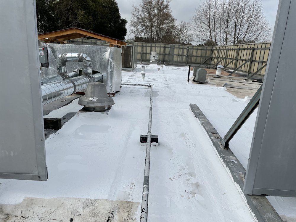 White-coated roof with metal equipment; a ventilation system with gray tubing. Cloudy day, outdoor setting.
