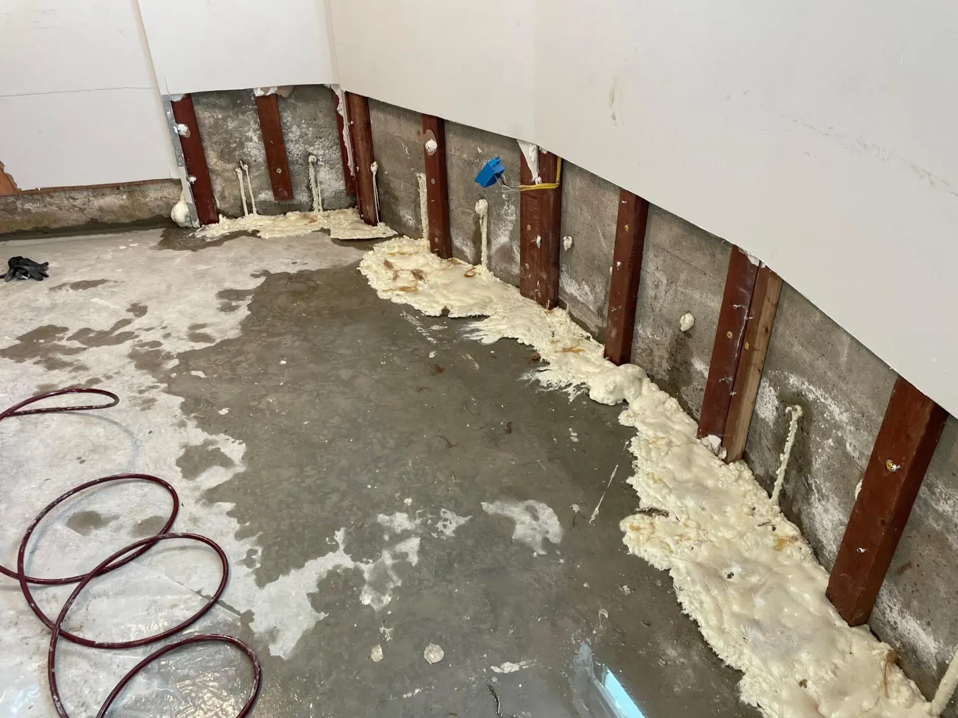 Interior view of a room under construction. Exposed concrete walls and floor with water pipes and insulation.