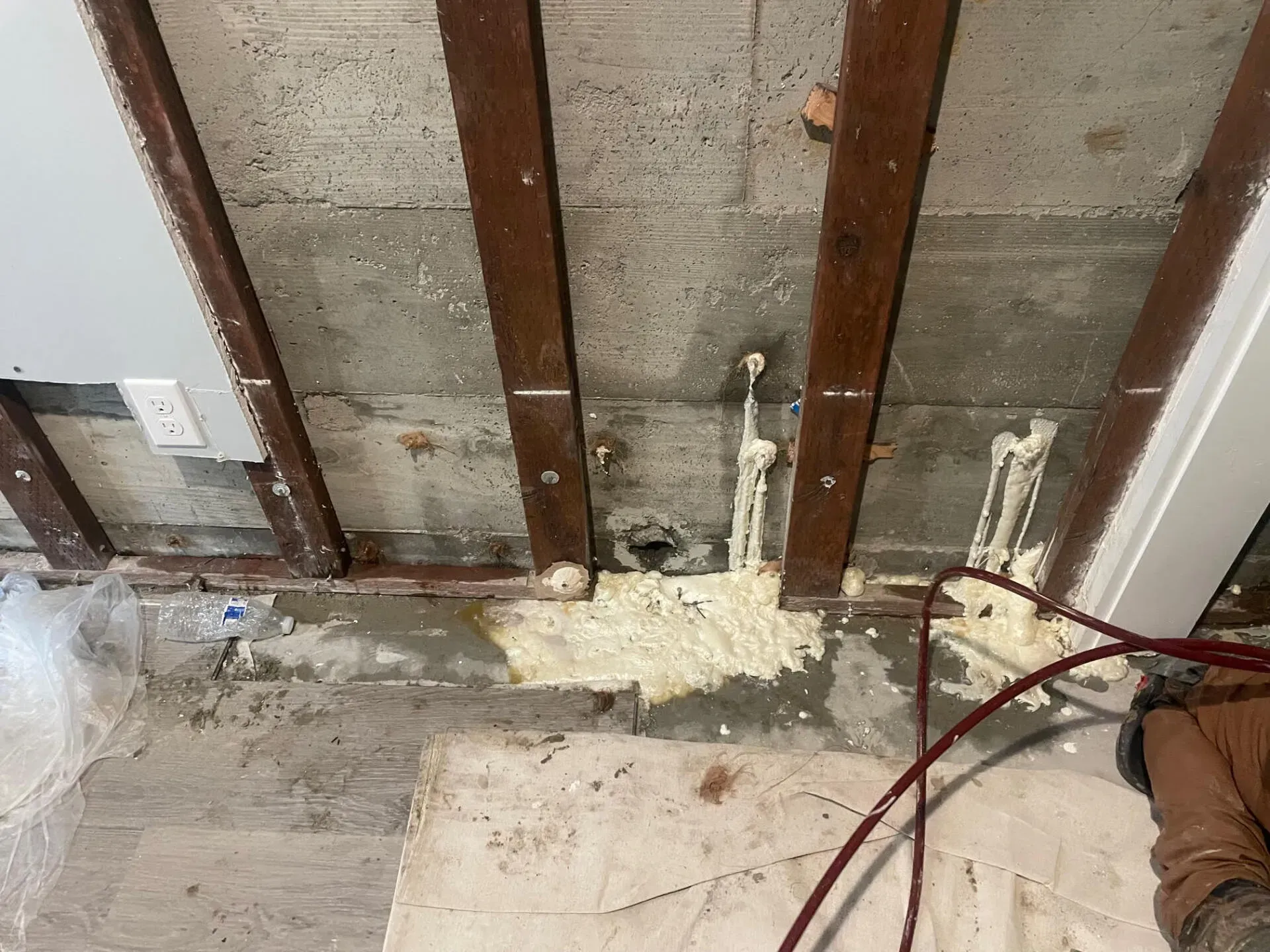 Foam insulation sprayed on a concrete ceiling and pipes in a room with exposed wooden beams and flooring.