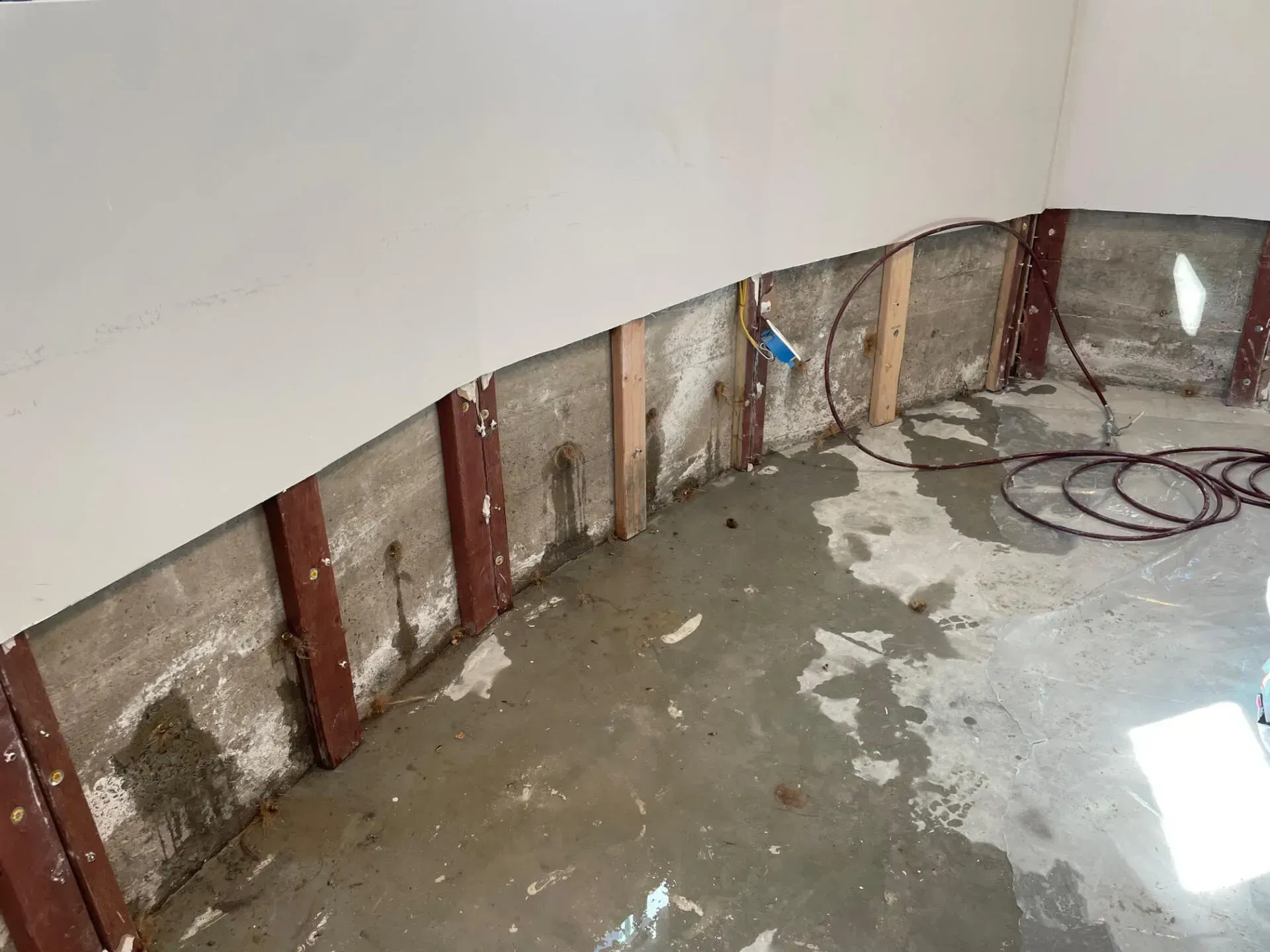 Concrete room with water damage, exposed wooden studs, and white walls.