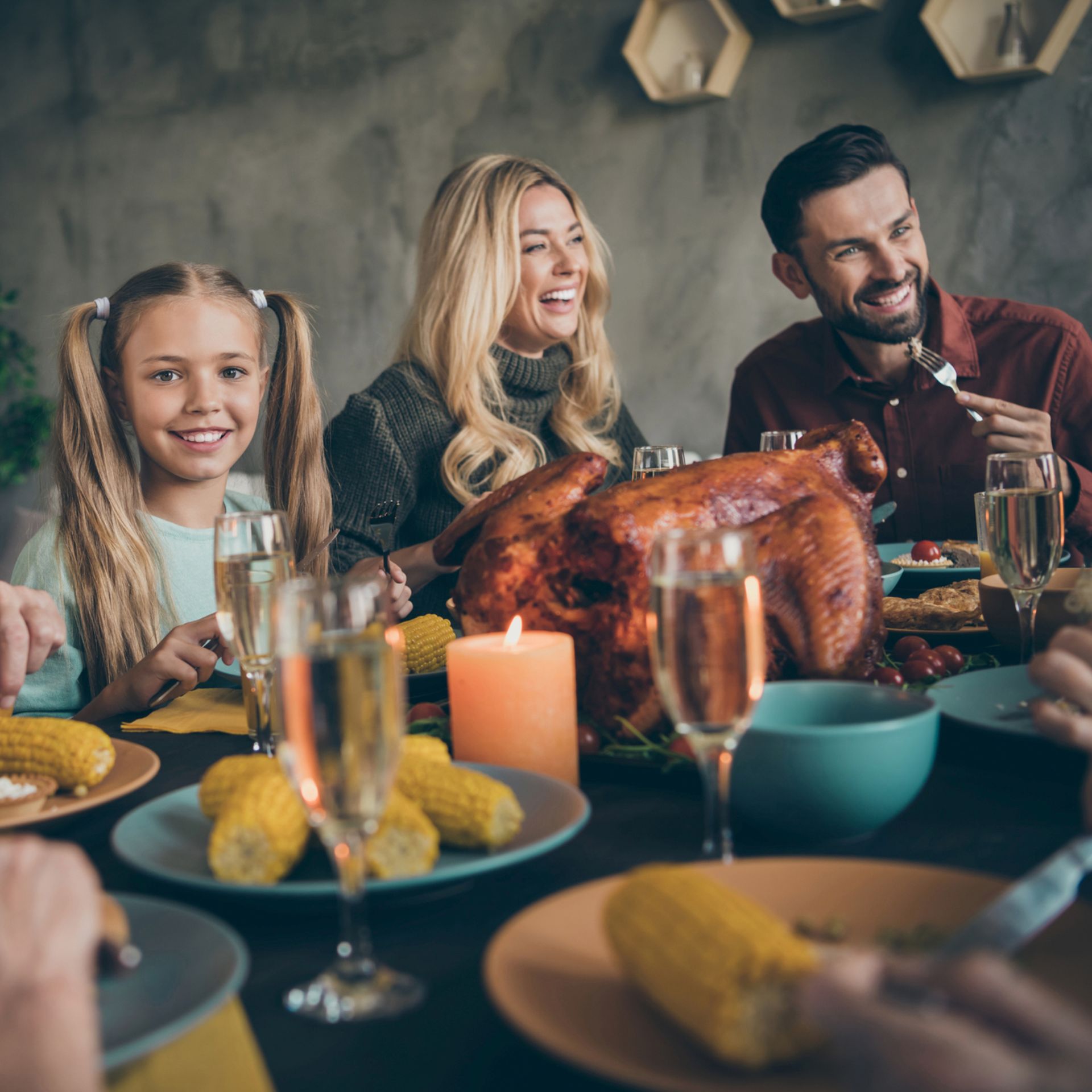 A family is sitting at a table with plates of food and a roasted turkey.