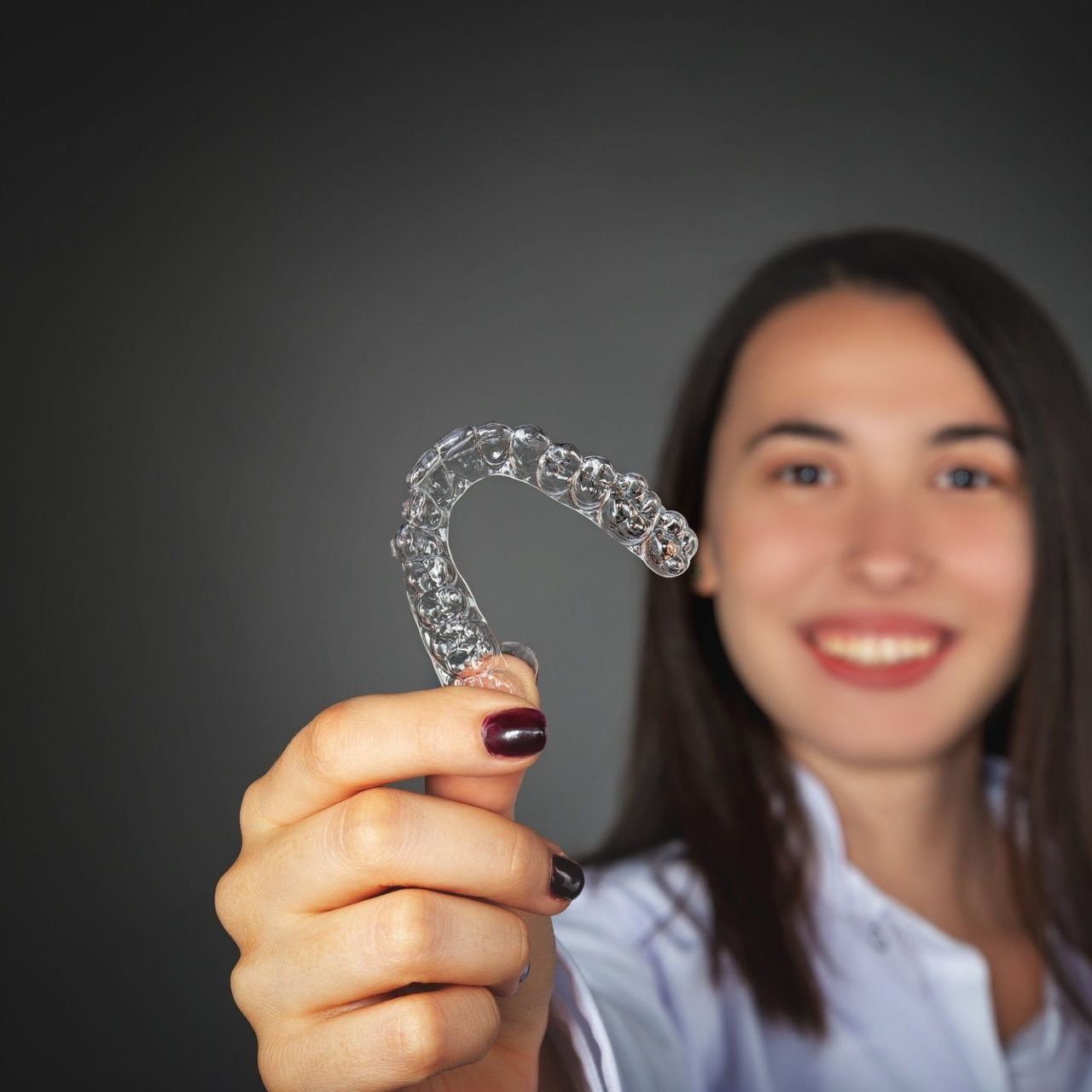 woman holding a clear aligner in front of her face