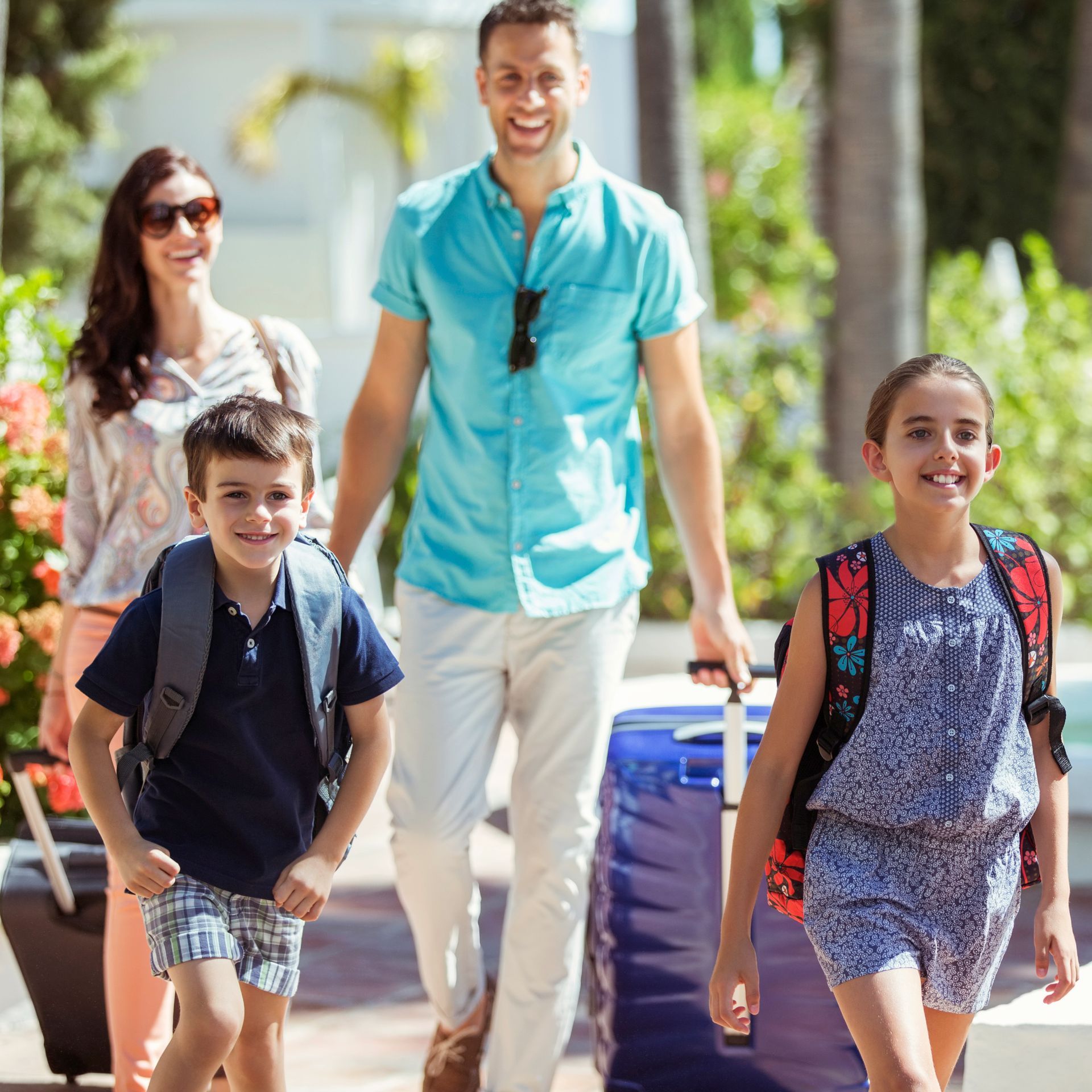 A family is walking down a sidewalk with luggage.