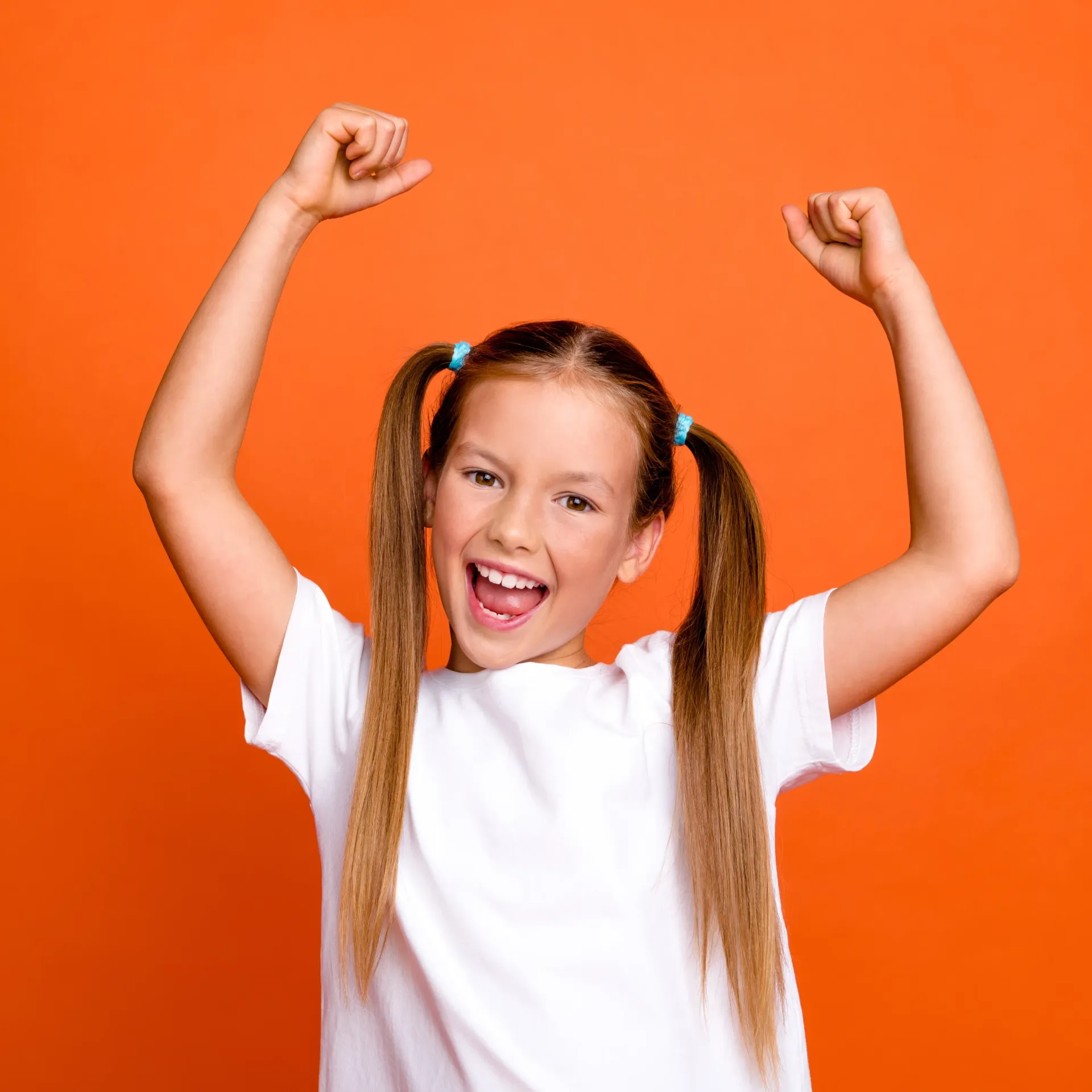 A young girl with pigtails is raising her arms in the air.