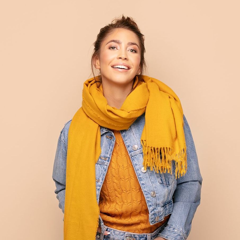 A woman wearing a yellow scarf and a denim jacket is smiling.