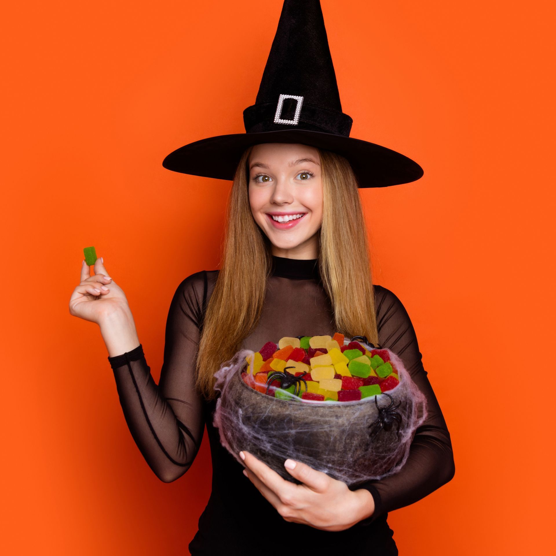 A woman in a witch costume is holding a bowl of gummy bears.