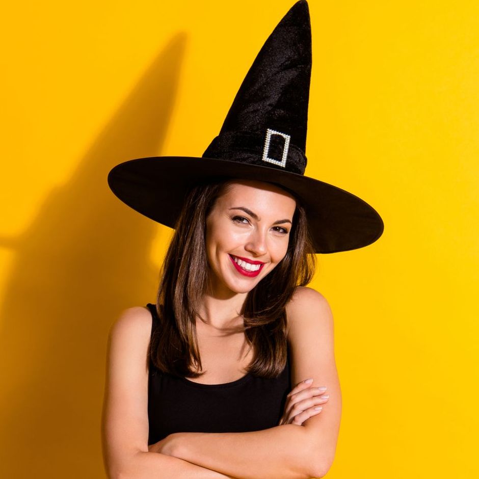 A woman is wearing a witch hat and smiling with her arms crossed.