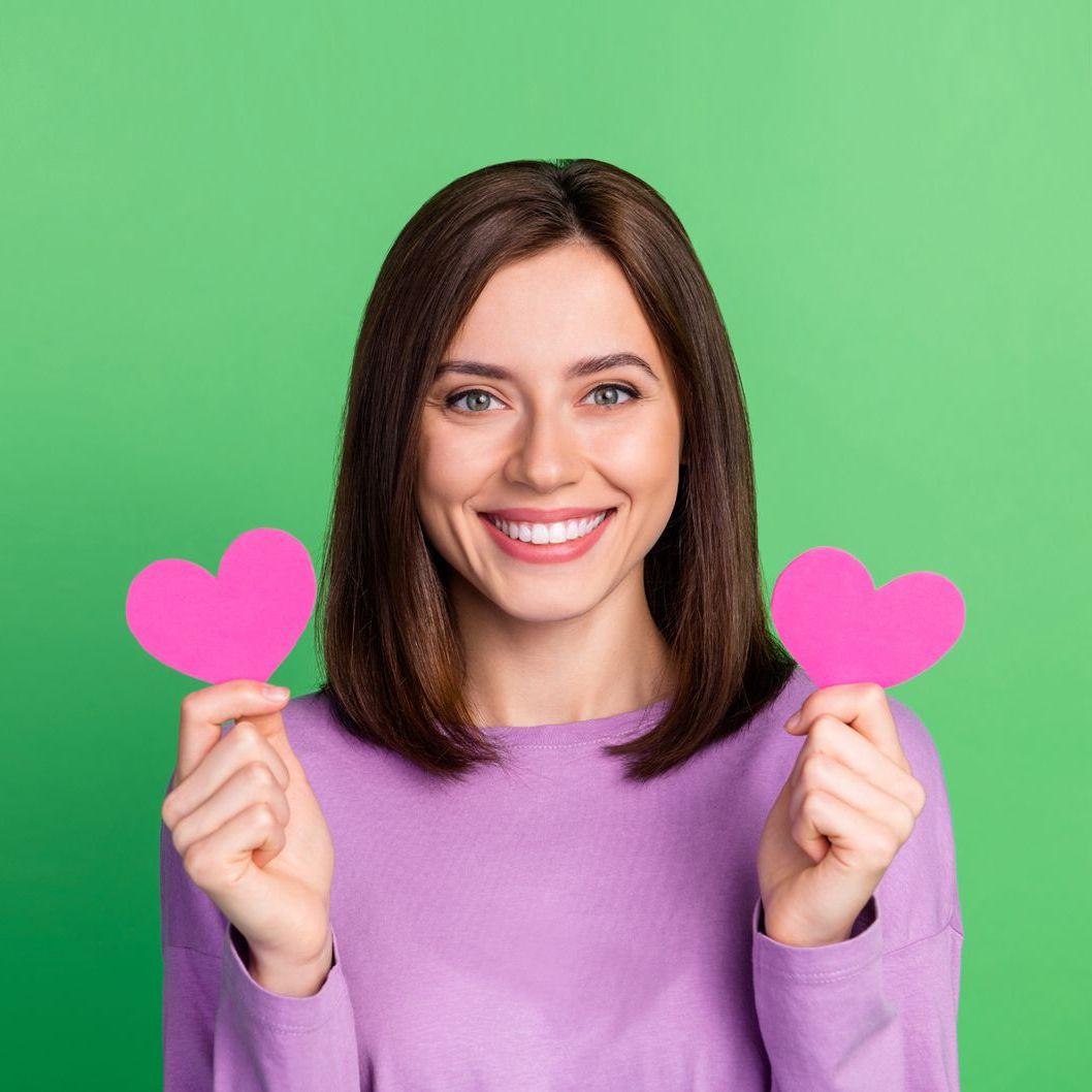 A woman in a purple sweater is holding two pink hearts in her hands.