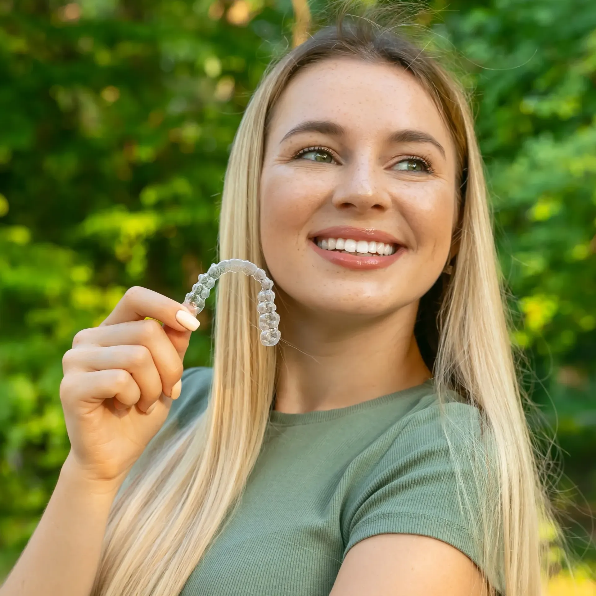 A woman is holding a clear brace in her hand and smiling.