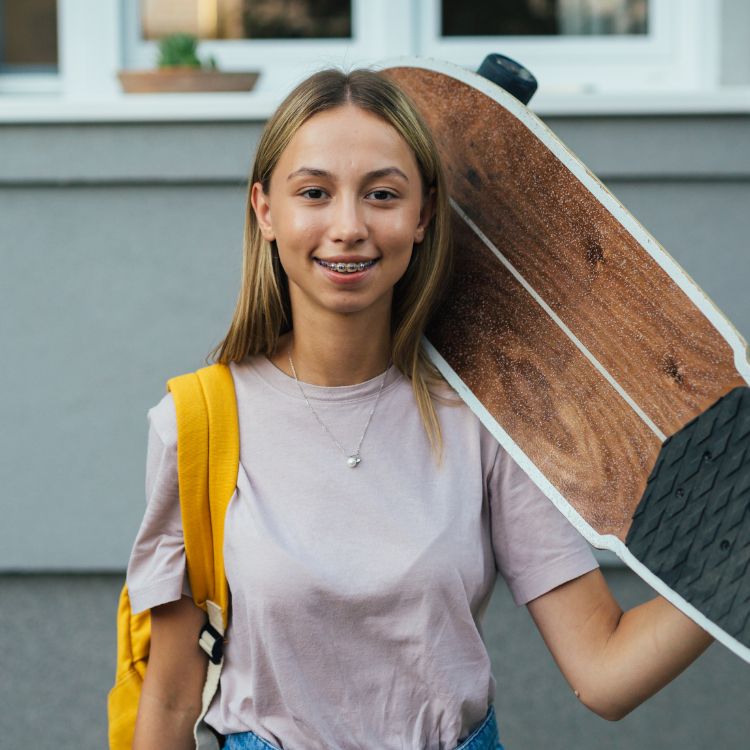 A woman with braces is holding a skateboard over her shoulder