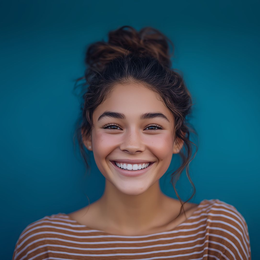 Young woman with a large smile, brown hair in a bun, against a teal background, wearing a striped shirt.