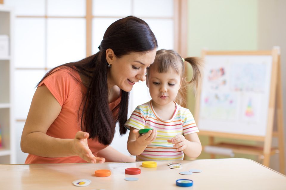 A woman and a little girl are playing with clay at a table.