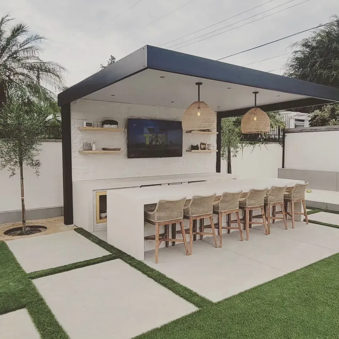 Outdoor kitchen and bar area with white countertops, wooden bar stools, and a black-roofed structure.