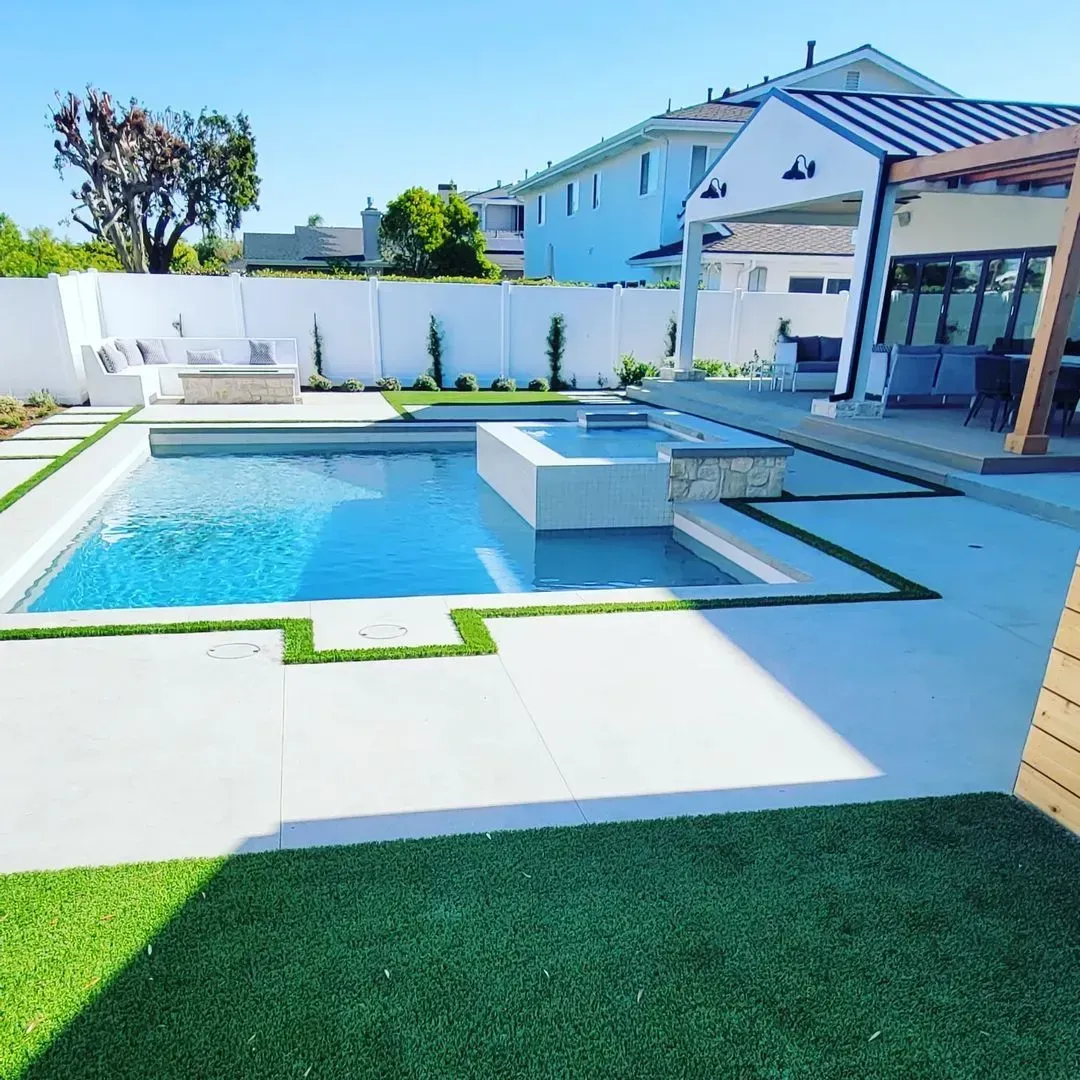 Backyard with a pool and spa, white fence, and modern house on a sunny day.