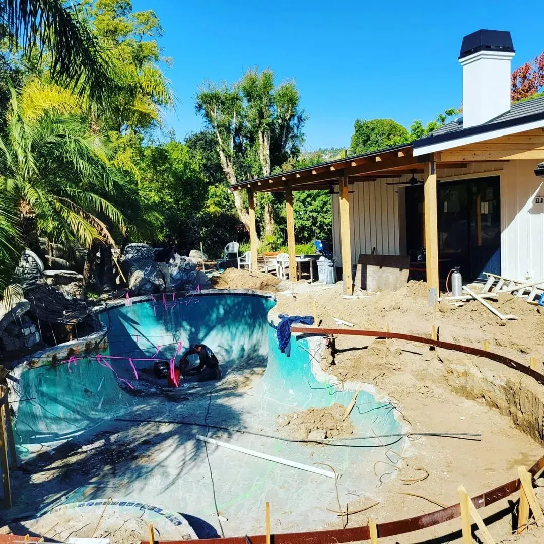 Pool under construction next to a house with a pergola, sunny day.