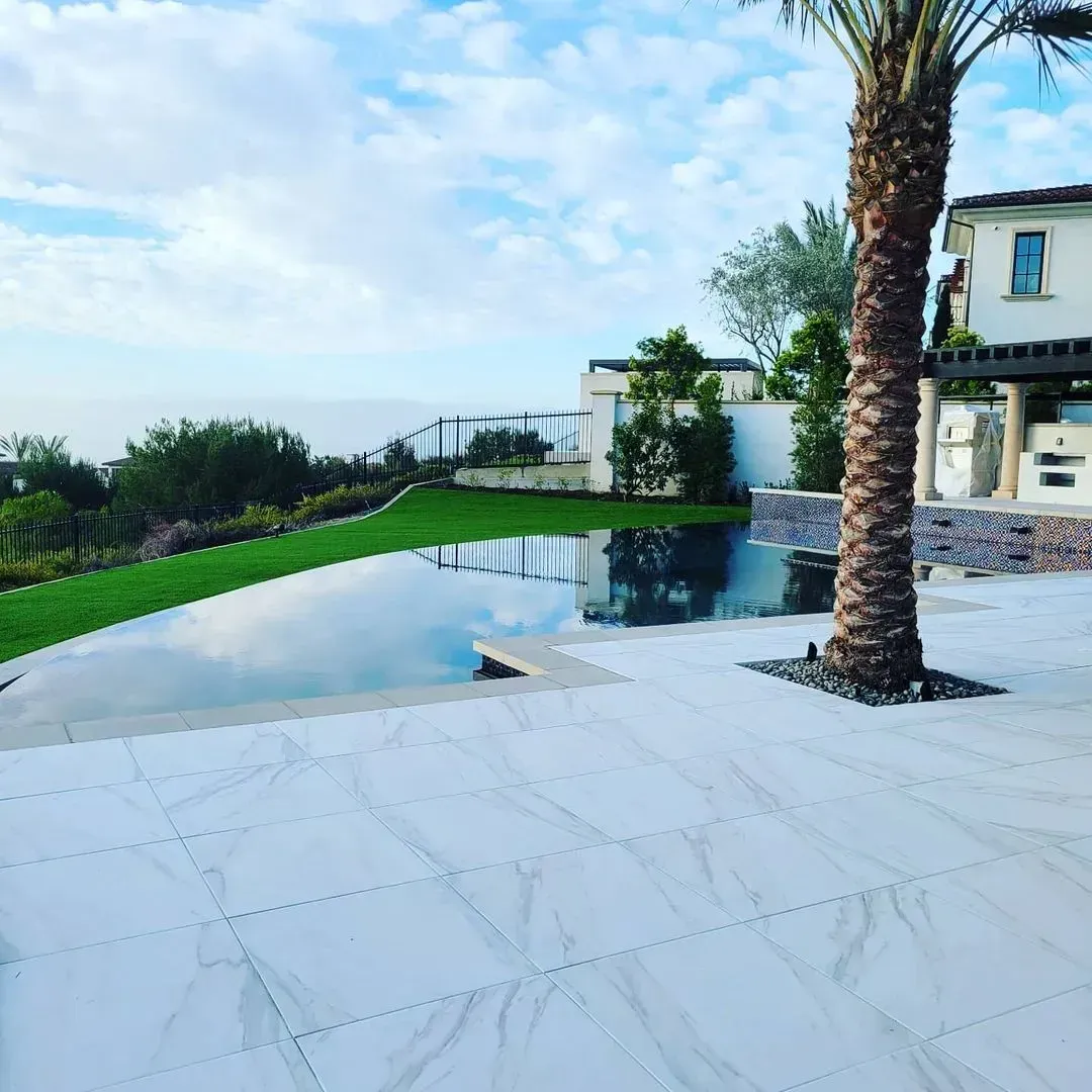 Poolside view with palm tree, lawn, and reflection of sky and buildings.