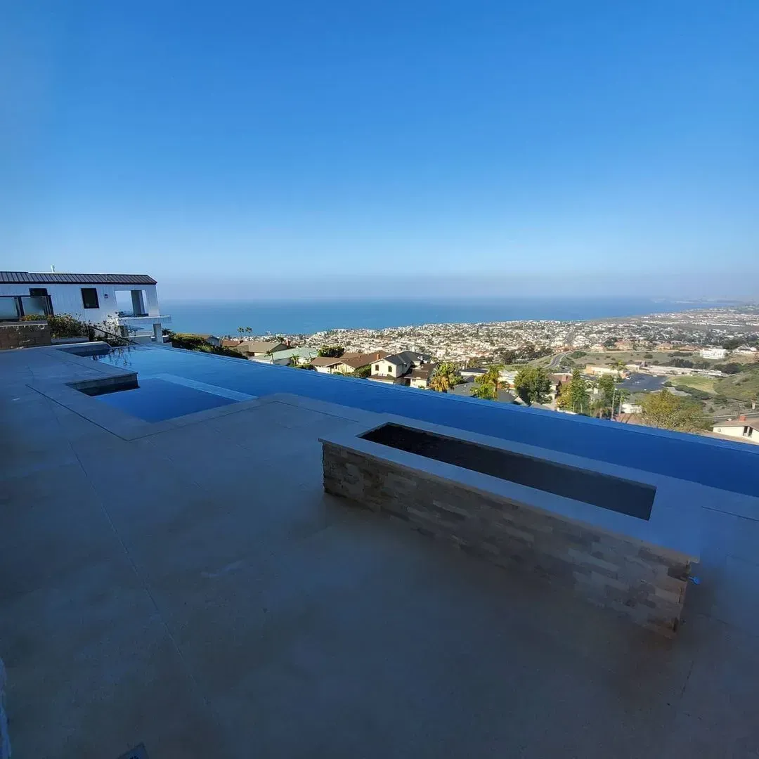 An infinity pool overlooks the ocean and a coastal city on a clear day.