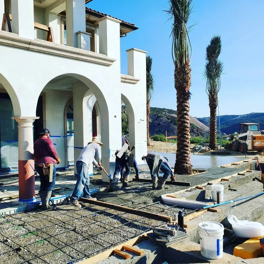 Construction workers pouring concrete at a house, under a sunny sky.