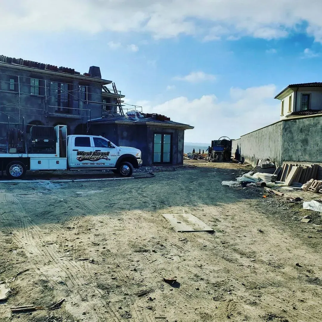 Construction site with a white work truck in front of a partially built house, with a blue sky.