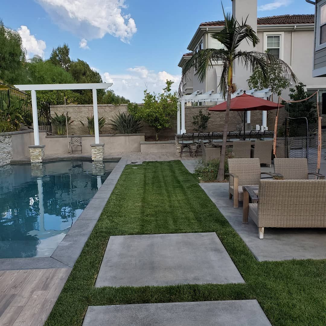 Backyard with pool, patio, and lawn. House in background, blue sky.