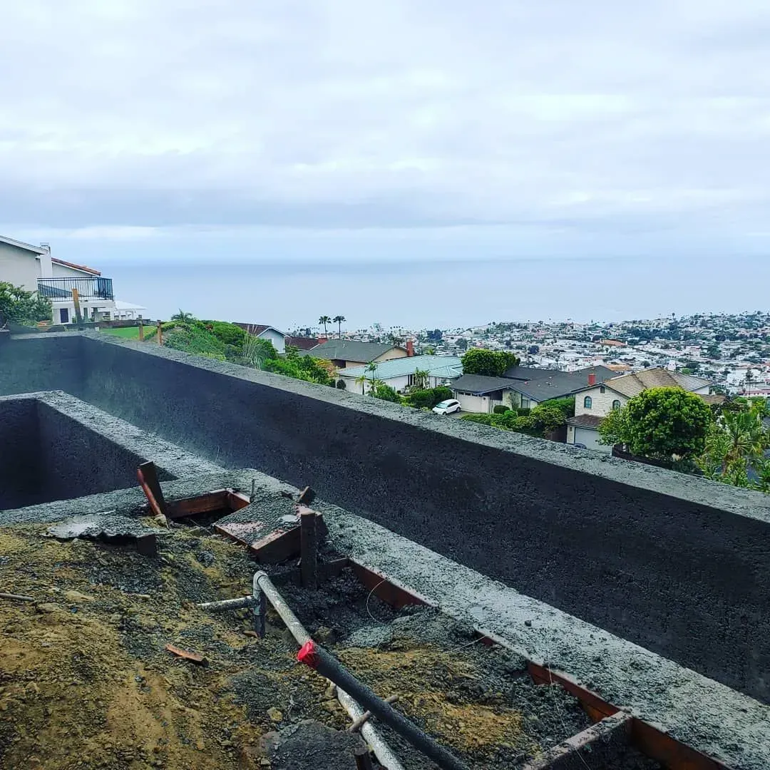 Construction site overlooking a coastal town. Concrete structure with ocean view, cloudy sky.
