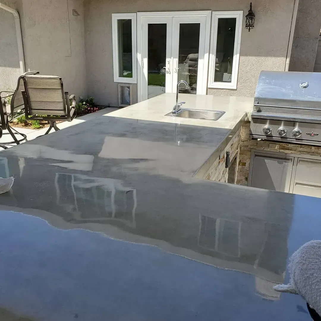 Outdoor concrete countertop with sink and grill. Patio setting with chairs and French doors.