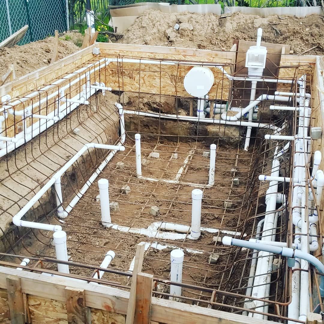 Construction of a rectangular pool: wooden frame, rebar, PVC pipes laid in the dirt.